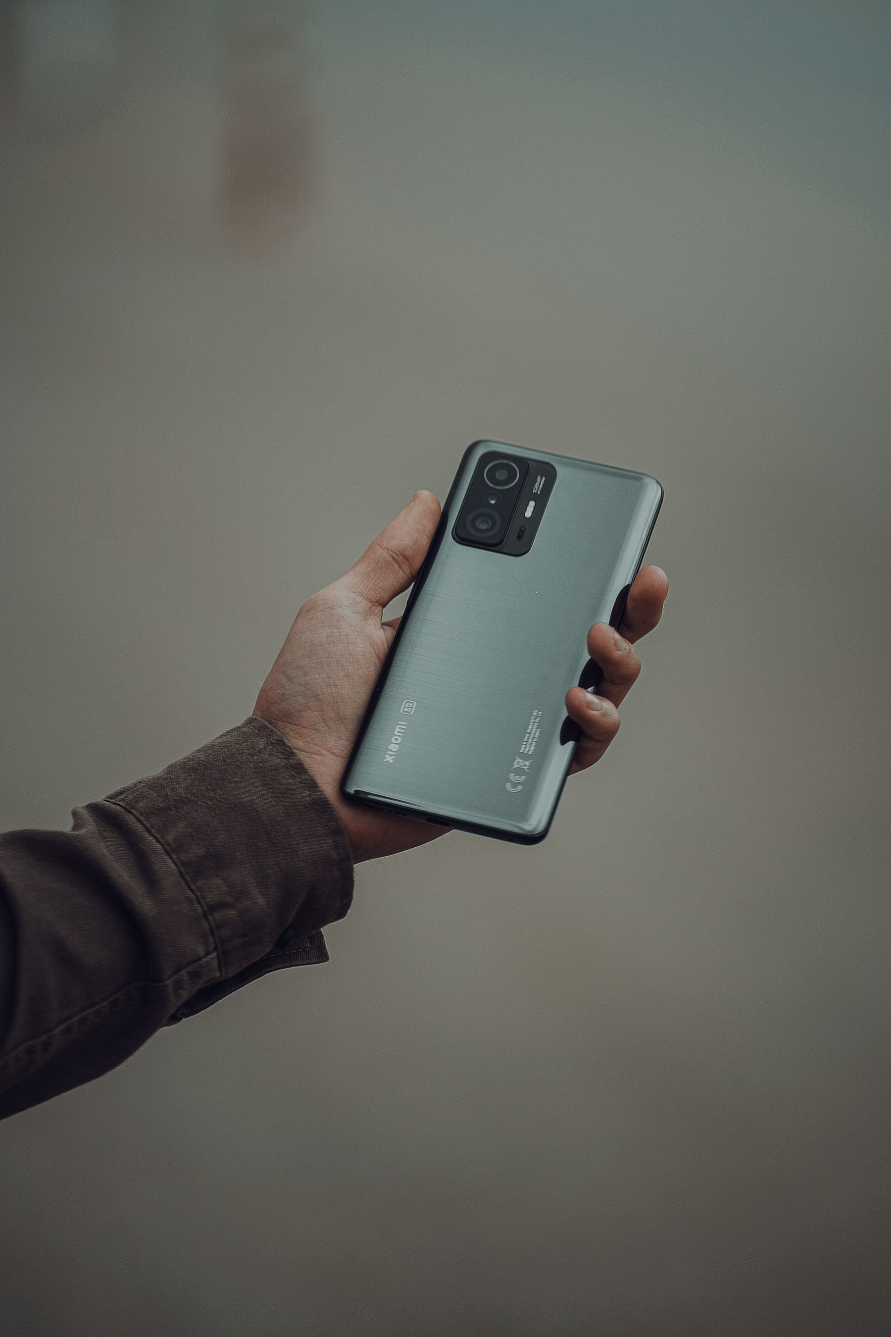 Close-up of a hand holding a modern smartphone against a grey background