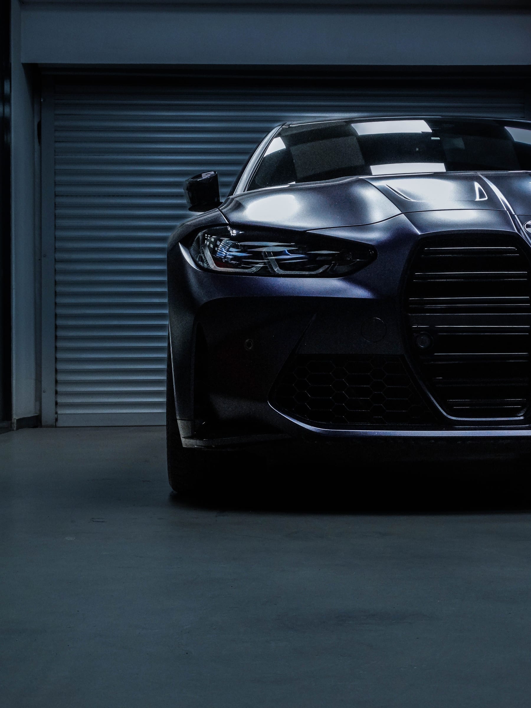 Black luxury sports car photographed front-on in a dimly lit garage